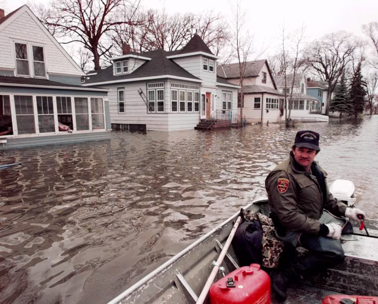 ** FILE ** Conservation Officer Keith Backer patrols an area of East Grand Forks, Minn., via boat April 29, 1997. Many East Grand Forks homes and businesses remained under floodwaters left by the Red River. The flooding river forced thousands to flee their homes iin Minnesota and neighboring Grand Forks, N. D. Ten years later, heavy rain and snow still make people nervous but a dike system has helped ease some fears. (AP Photo/Eric Gay)