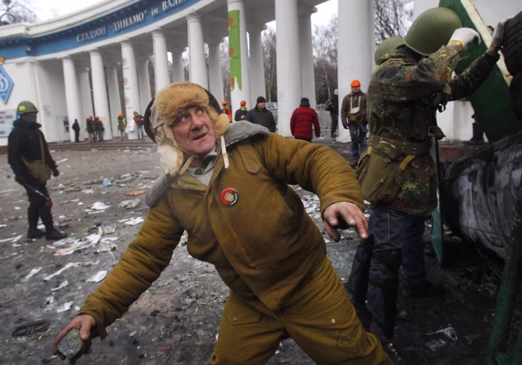 Image: An elderly protester prepares to throw a stone, during clashes with police, in central Kiev
