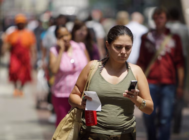 Image: A woman uses her cell phone to text message while walking.