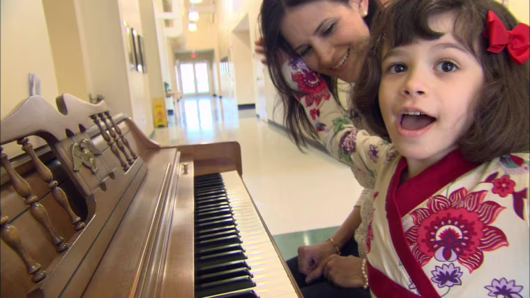 Kim Cristo sits at a piano with her daughter Ava, 6. Kim credits the intervention Ava has received at REED Academy in Oakland, N.J., for helping her overcome some of the language deficits caused by autism.