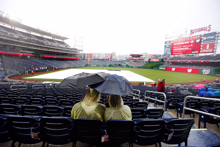 Image: Fans sit under umbrellas in the rain before an exhibition baseball game between the Washington Nationals and the Detroit Tigers at Nationals Park Saturday