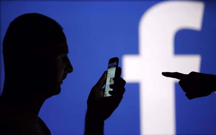 Image: Man silhouetted against video screen with Facebook logo