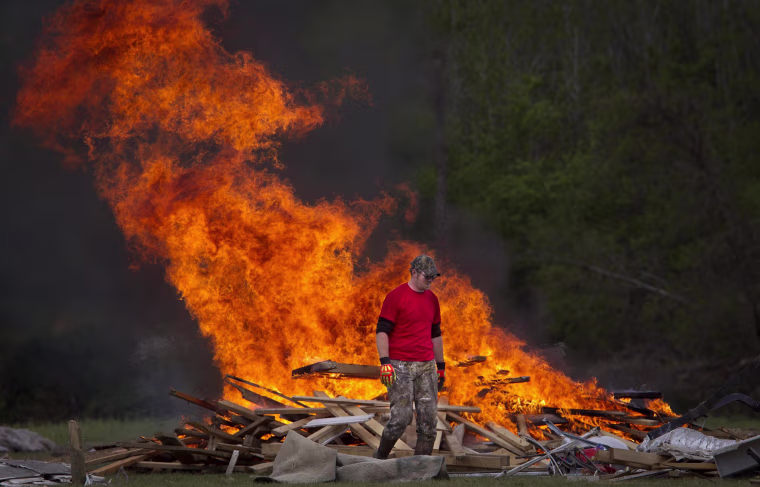 Image: Man walks away from a clean-up debris fire in Vilonia, Arkansas