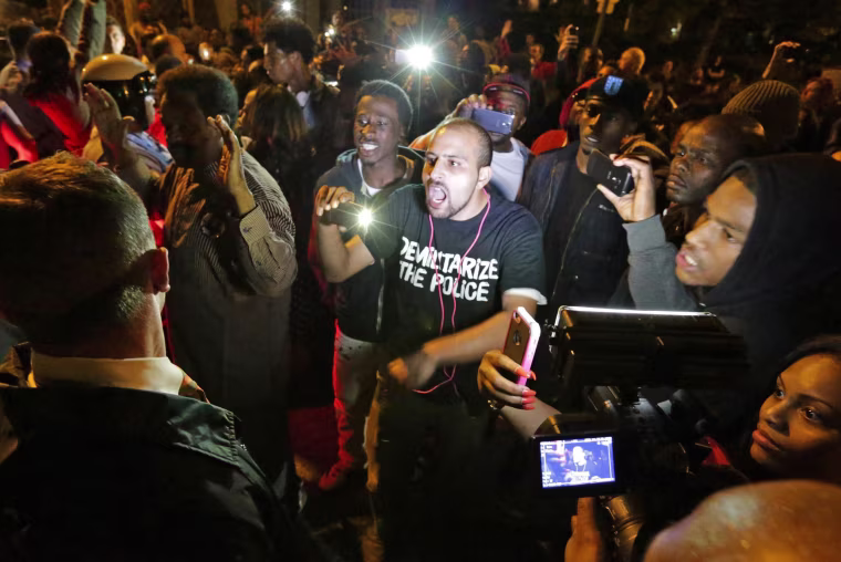 Image: Crowds confront police near the scene in south St. Louis where a teen was fatally shot by an off-duty police officer