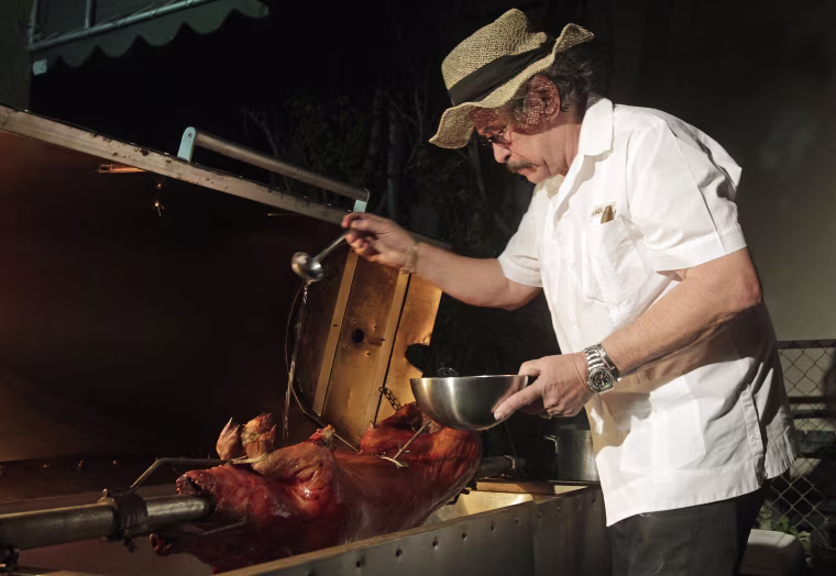 Image: Chef's Paella chef, Jorge Suarez, also known as "Chino" Chef Paella, who specializes in slow cooked pork, puts the finishing touches on an animal as it slow cooks in Paella's portable cooker at the customer's home in Miami, Florida