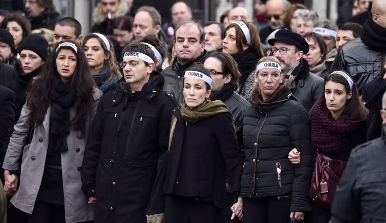 Image: Cartoonist Corinne Rey (3rd left in green scarf) known as Coco, a survivor of the attack on the Charlie Hebdo satirical magazine, and other staff members, link arms as the take part in a Unity rally "Marche Republicaine" on January 11, 2015 in Pari