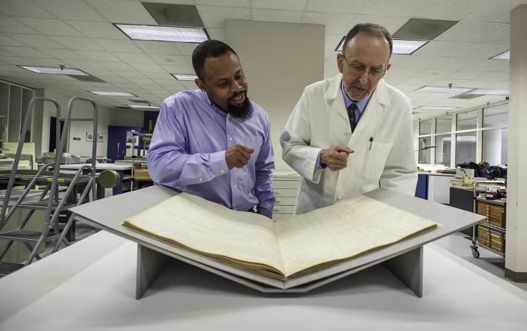 Image: At the National Arhives, Damani Davis, Reference Archivist and Steven Loew, Conservator, discuss the conservation and historical significane of the Book of Negroes.