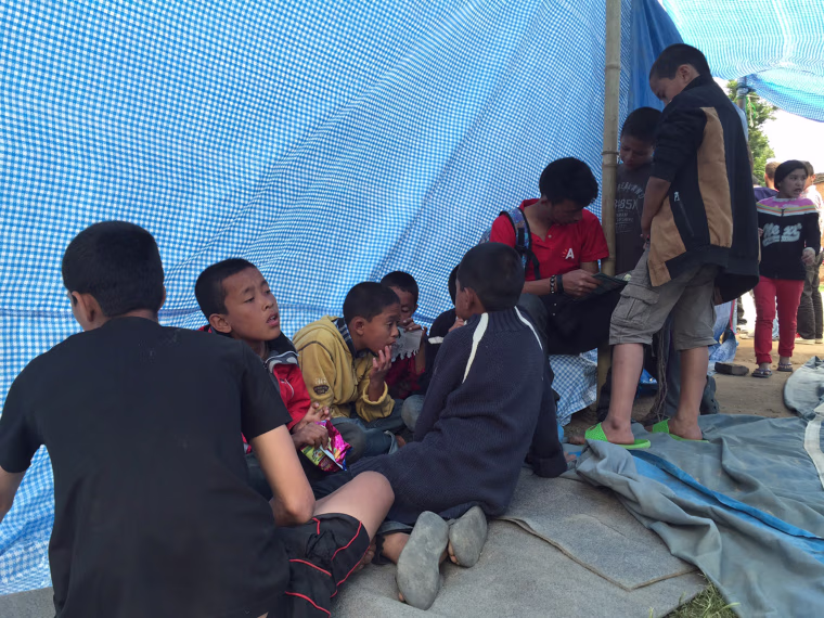 Children underneath the tarp in the yard next to the house where they have taken shelter.