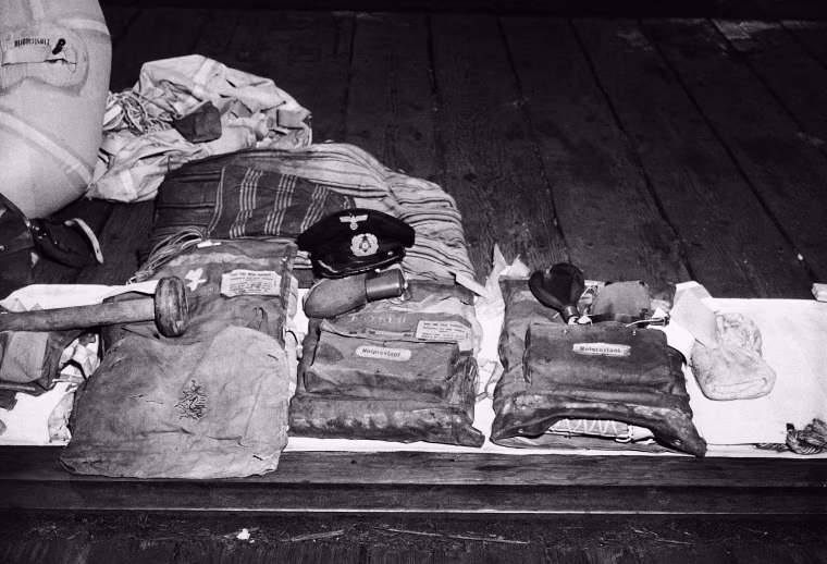All that has come in from the Nazi Sub U-853, which torpedoed a collier off Pont Judith, R.I., shortly before the German Capitulation, is this assortment of wreckage and clothing. Included above are the captain’s cap, artificial lungs, a mattress and pillow, a liferaft, a towel, and what appears to have been part of her flagstaff. The sub was destroyed by depth charges dropped in shallow water by the USS Atherton, a destroyer escort shown May 16, 1945.