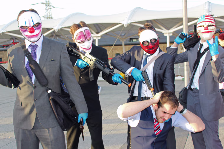 A kneeling man pretends to be a bank manager as he's surrounded by attendees dressed as characters from the video game "Payday" at MCM Comic Con in London. The event required attendees to place orange or red caps on the muzzle of plastic pistols and rifles.