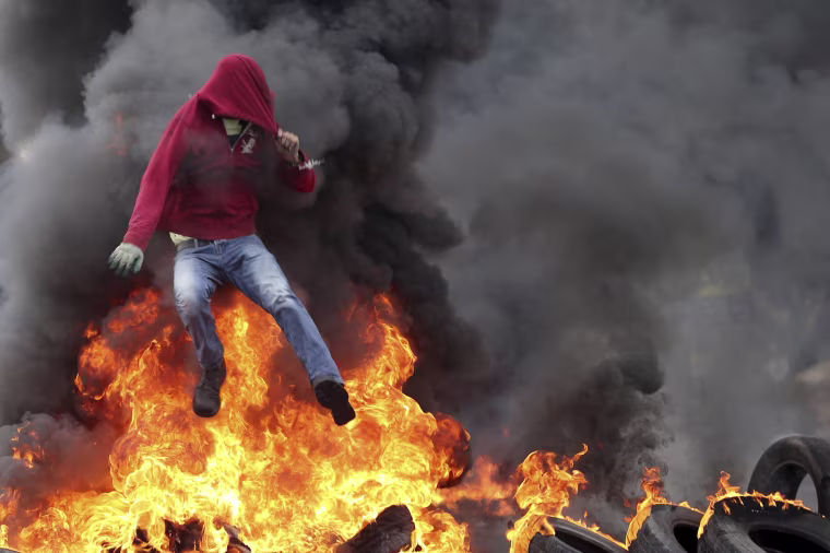Image: Palestinian protester jumps over burning tyres during clashes with Israeli troops near the Jewish settlement of Bet El, near the West Bank city of Ramallah
