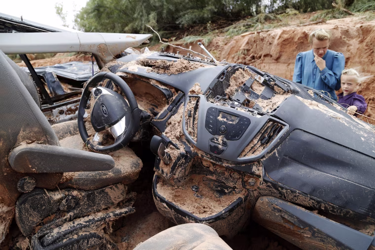 Image: A woman and child examine a vehicle swept away during a flash flood
