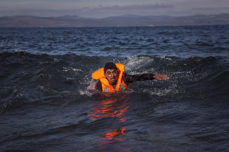 Image: A migrant swims as he arrives on the island of Lesbos after crossing the Aegean sea