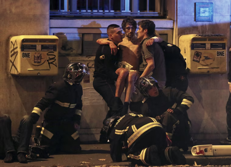Image: French fire brigade members aid an injured individual near the Bataclan concert hall