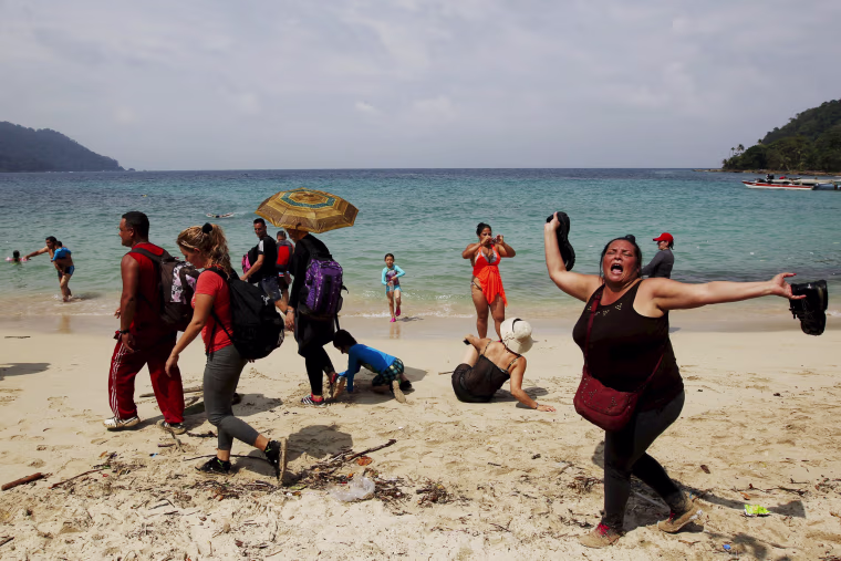 Image: A Cuban migrant shouts \"Cuba\" after arriving to the beach after crossing the border from Colombia through the jungle as tourist stand by in La Miel, in the province of Guna Yala, Panama