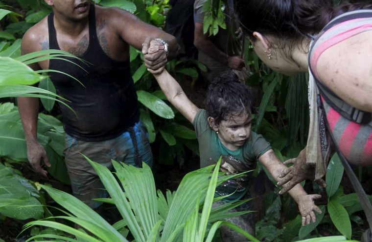 Image: Cuban migrants help a child as they walk down crossing the border from Colombia through the jungle into La Miel, in the province of Guna Yala, Panama