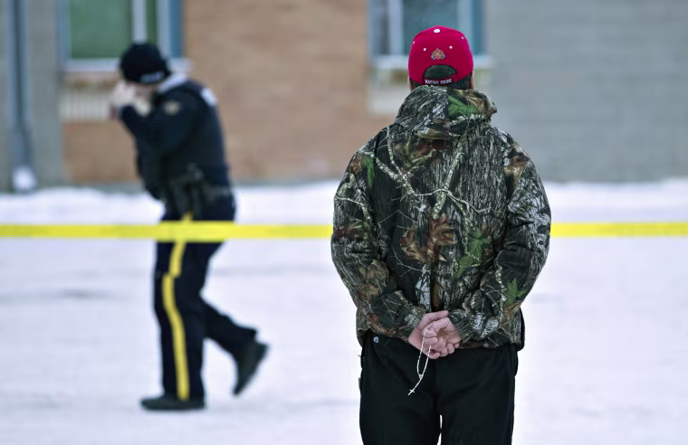 A man holds a rosary as police investigate the scene of a shooting at the community school in La Loche, Saskatchewan, on Saturday, Jan. 23, 2016, a day after the violence.