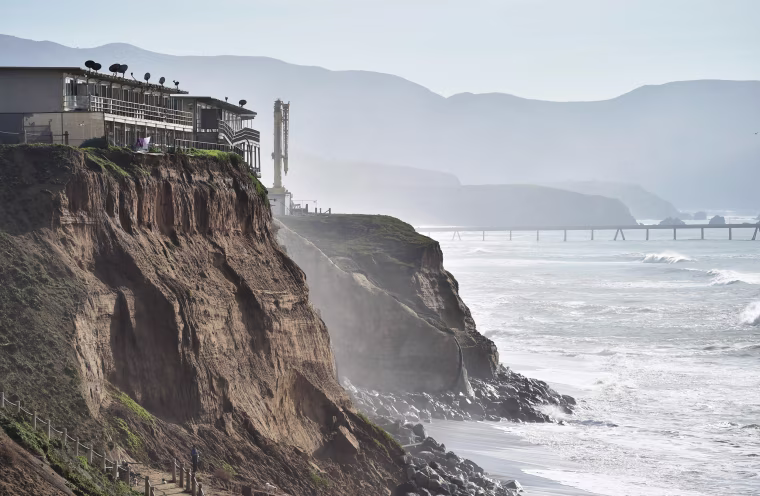 Image: Apartments are seen at the edge of an eroding cliff while residents evacuate in Pacifica