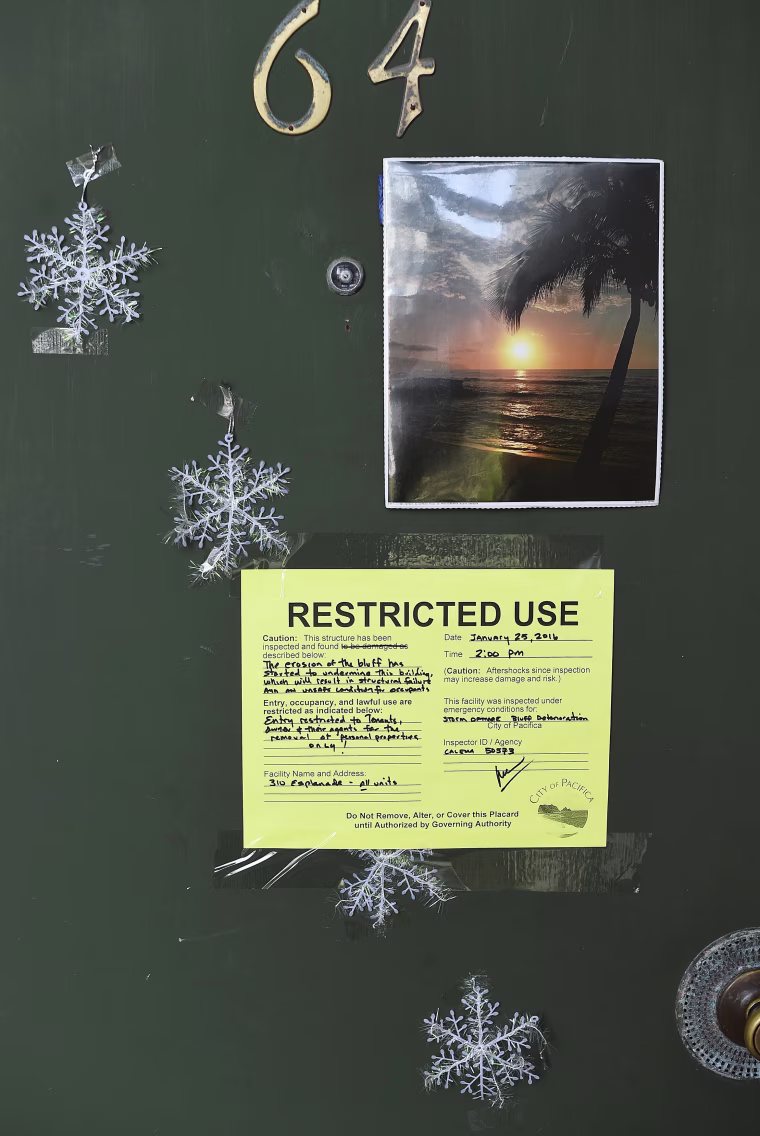 Image: A warning notice is pictured on a door at an uninhabitable apartment, in danger of collapsing due to storm erosion, in Pacifica