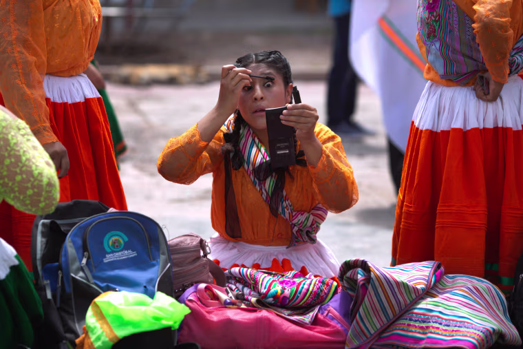 Image: Andean woman in traditional dress, applies mascara before the carnival in Ayacucho