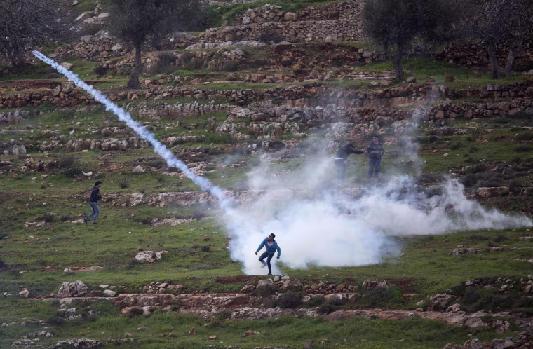 Image: A Palestinian demonstrator throws back a tear gas canister that was fired by Israeli troops during demonstration