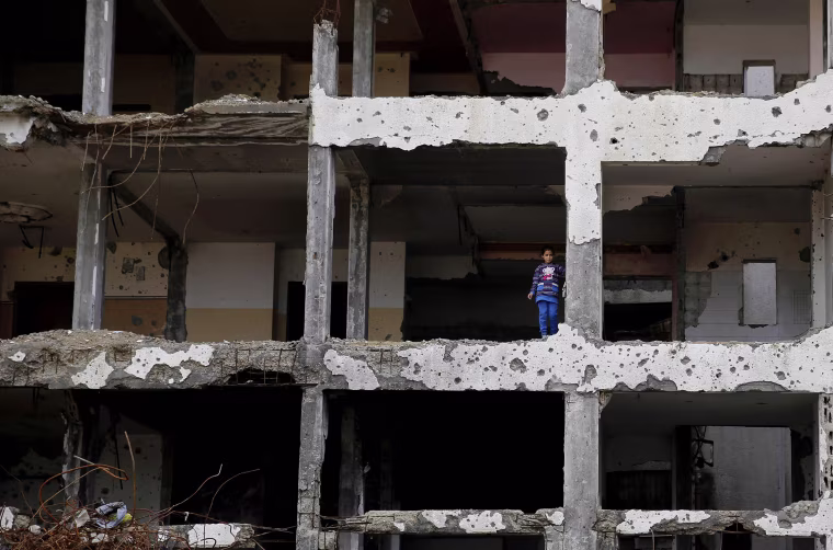 Image: A Palestinian girl stands on a floor of a damaged apartment block