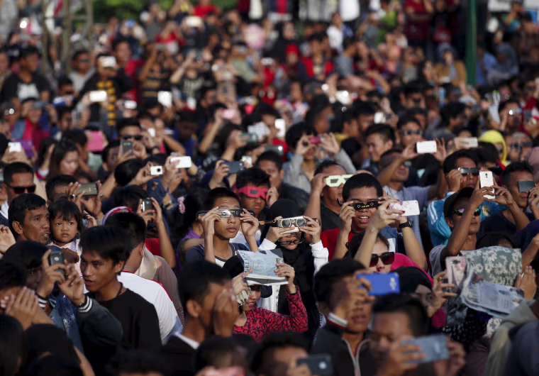 Image: People watch a solar eclipse near the Ampera Bridge along the banks of the Musi River in Palembang, South Sumatra province, Indonesia