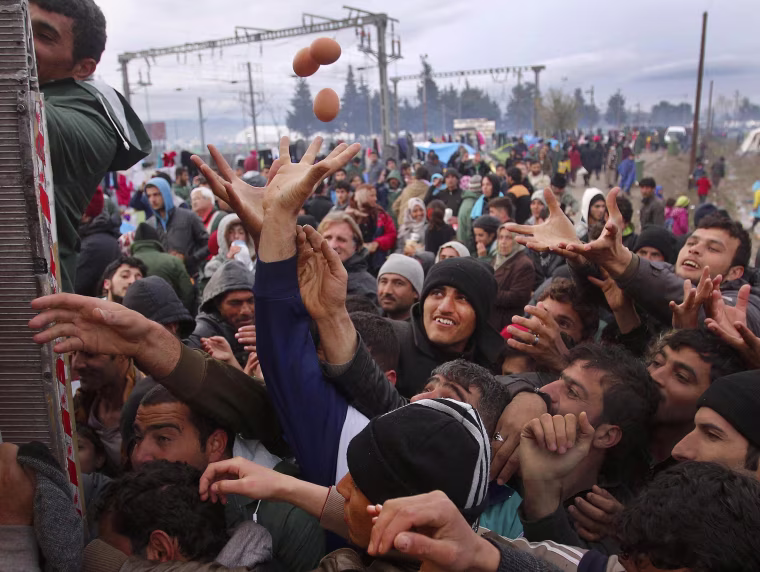 Image: Migrants try to get products from a truck at a makeshift camp on the Greek-Macedonian border near the village of Idomeni