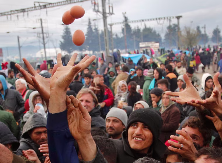 Image: Migrants try to get products from a truck at a makeshift camp on the Greek-Macedonian border near the village of Idomeni