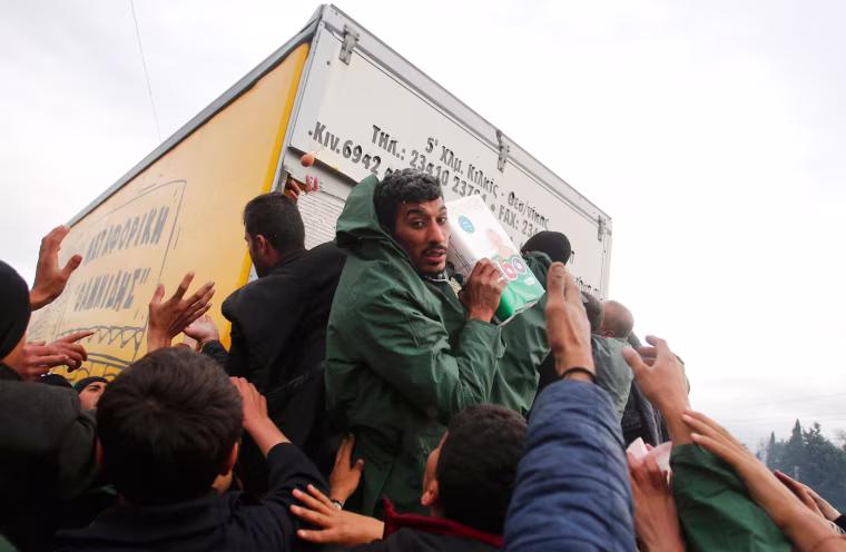 Image: Migrants try to get products from a truck at a makeshift camp on the Greek-Macedonian border near the village of Idomeni