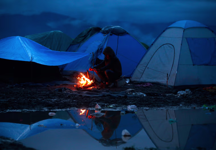 Image: Migrant warms up by a fire at a makeshift camp on the Greek-Macedonian border, near the village of Idomeni