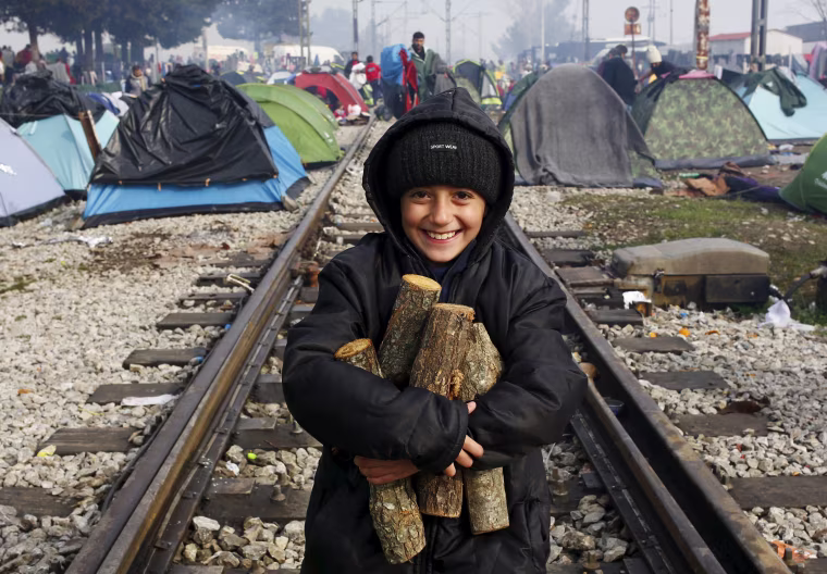Image: A migrant child, waiting to cross the Greek-Macedonian border, carries firewood along a railway track during a foggy early morning near the village of Idomeni
