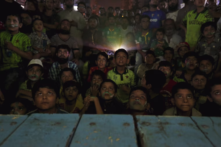 Image: Young Pakistani cricket fans look at a screen along a roadside in Karachi, Pakistan
