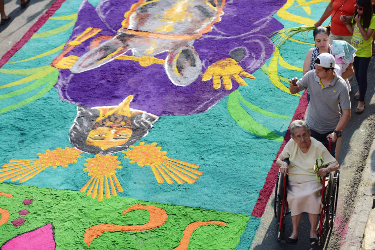 Image: Catholic faithful walk by a sawdust carpet as they take part in the Palm Sunday celebrations