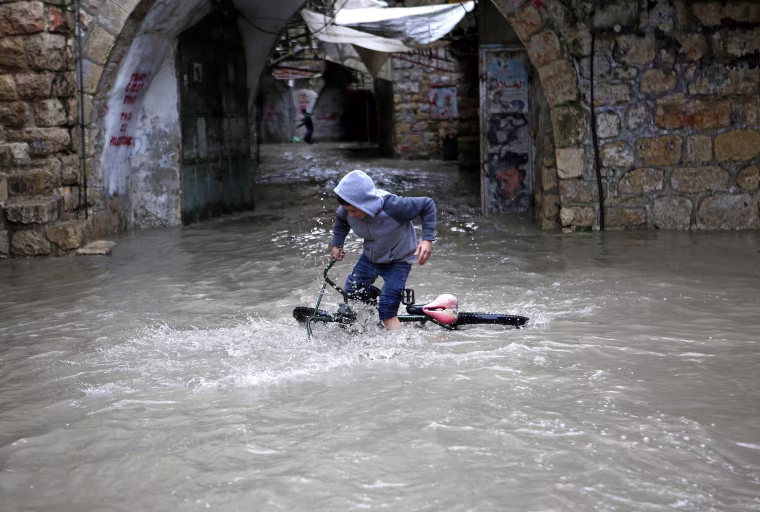 Image: A Palestinian boy tries to ride his bicycle through flood water