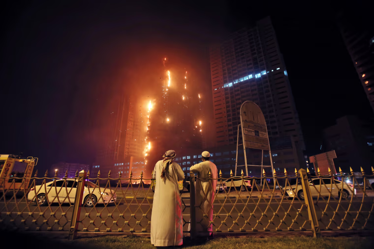 Image: Two Emirati officials watch a high-rise building as a fire spreads up the side of the building in Ajman