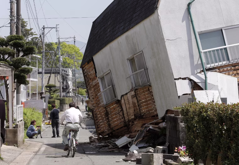 Image: A man cycles past a collapsed house