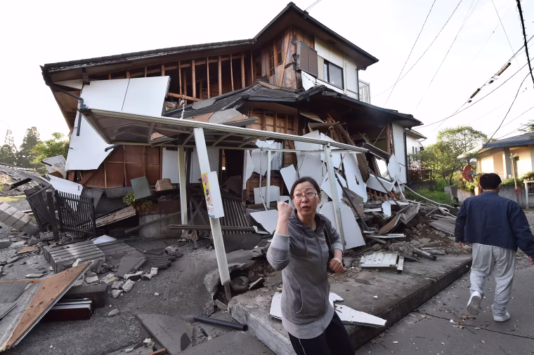 Image: A couple heads to their home past a collapsed house