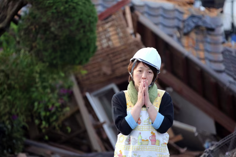 Image: A residents stands in front of a damaged house in Mashiki