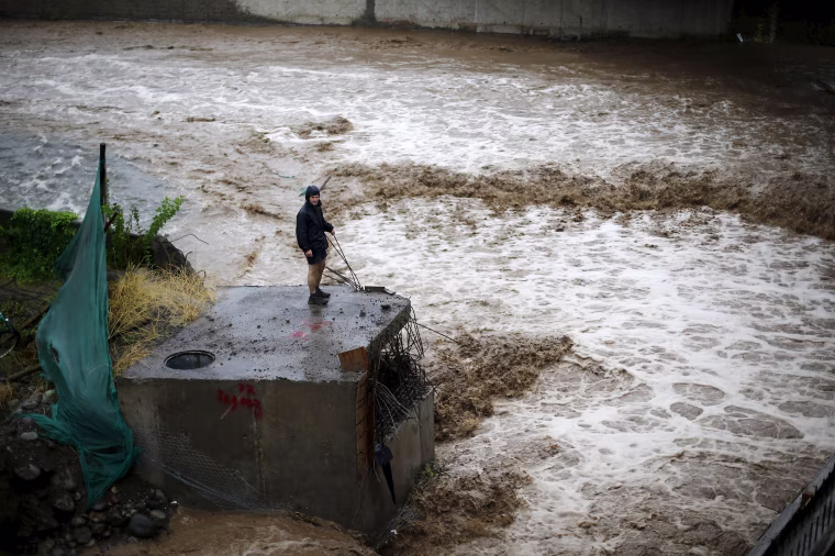 Image: A man is seen next to a river during floods in Santiago
