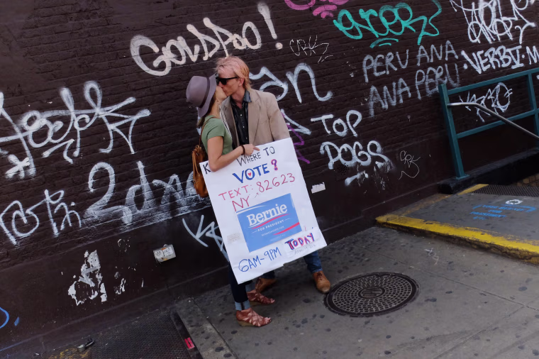 Image: A couple shares a kiss as they hold a sign to promote the vote for Bernie Sanders
