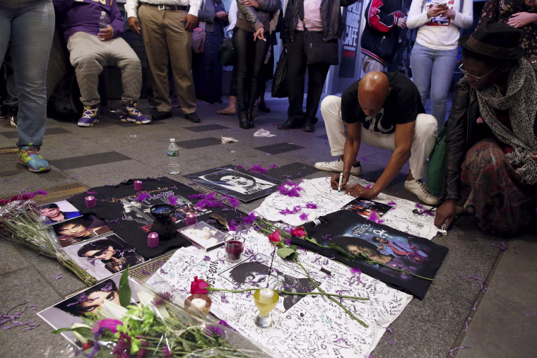 Image: A man writes on a makeshift memorial as fans gather at Harlem's Apollo Theater to celebrate the life of the deceased musician in New York