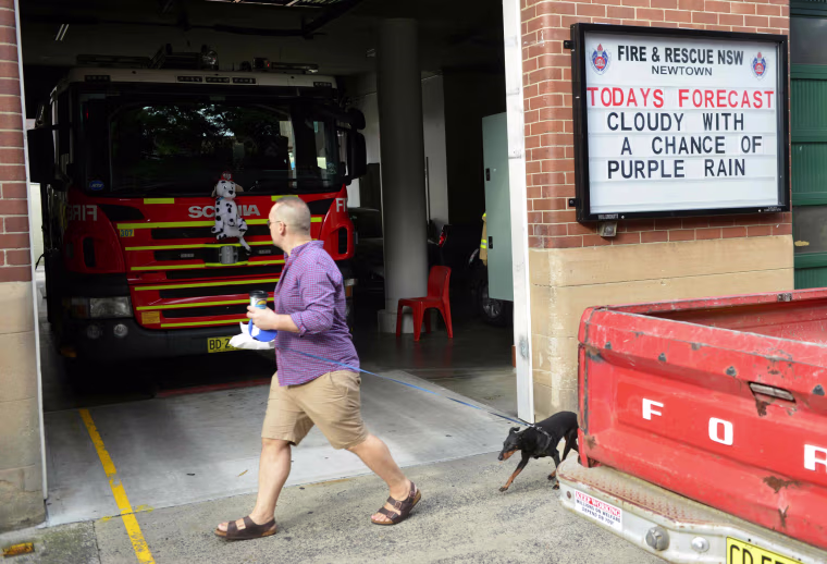 Image: A pedestrian walks past a fire station in Sydney with a tribute message displayed