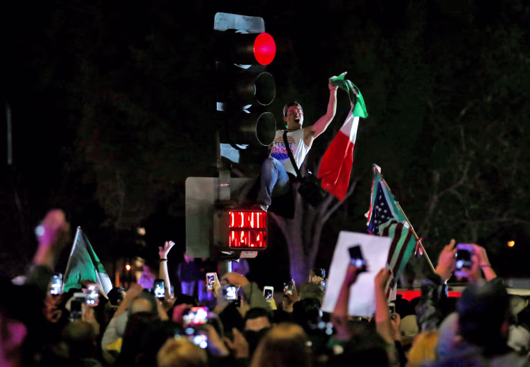 Image: A demonstrator climbs a traffic light outside Republican U.S. presidential candidate Donald Trump's campaign rally in Costa Mesa