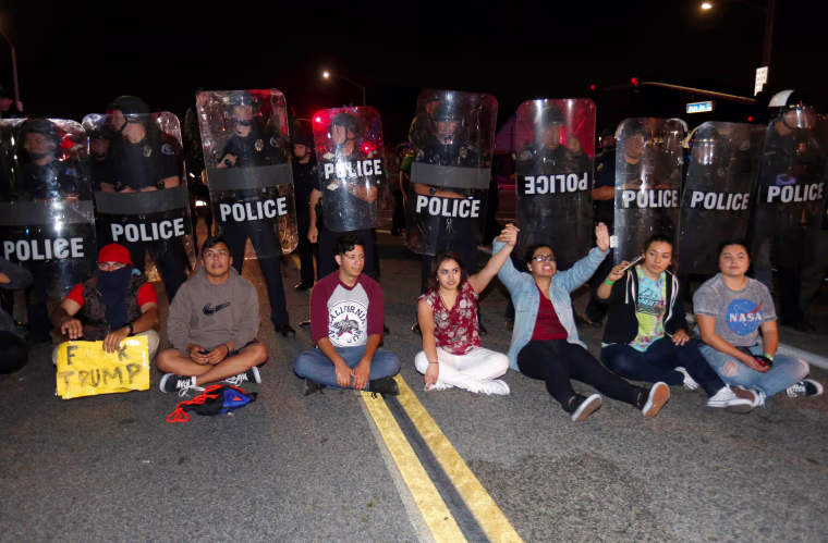 Image: Demonstrators sit in front of a line of police in riot gear outside Republican U.S. presidential candidate Donald Trump's campaign rally in Costa Mesa, California