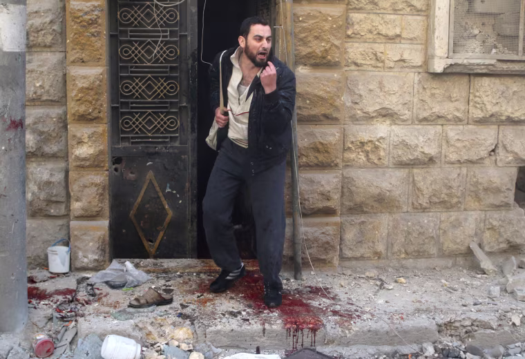Image: A man reacts as he stands on blood stains at a site hit by airstrikes in the rebel held area of Aleppo's al-Fardous district
