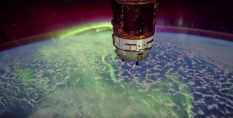 The International Space Station passes over an aurora at the edge of the Earth's atmosphere.