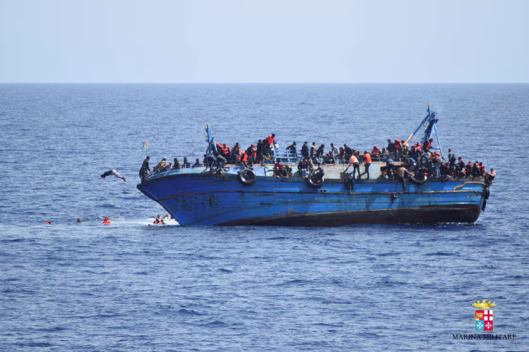 Image: Migrants are seen on a capsizing boat before a rescue operation by Italian navy ships \"Bettica\" and \"Bergamini\" (unseen) off the coast of Libya