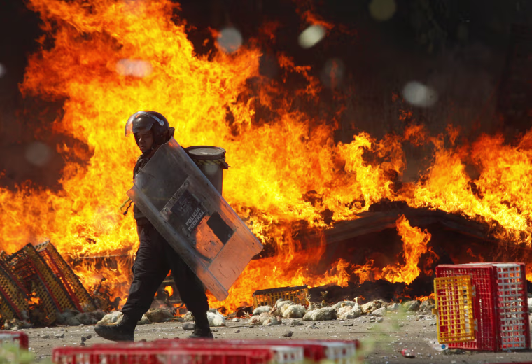 Image: A riot police officer walks past a burned truck carrying chickens after clash with protesters from the National Coordination of Education Workers (CNTE) teachers???????? union during a protest, in Nochixtlan