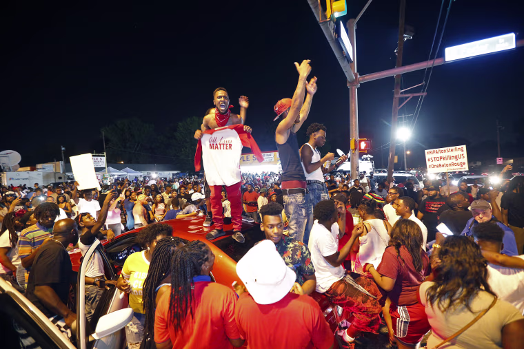 Image: Protesters stand on cars as they congregate in Baton Rouge